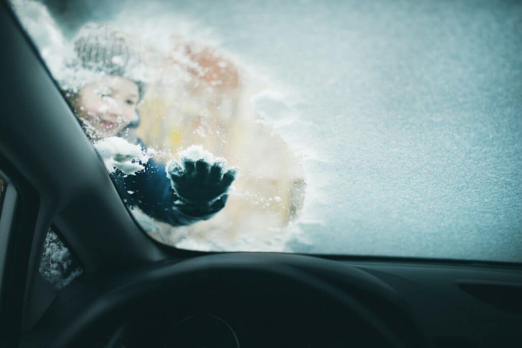 The girl helps her parents and cleans the windshield of the car. Household chores in winter.